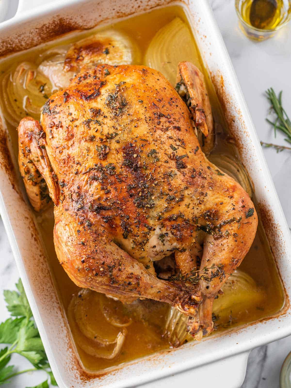 Roasted whole chicken with golden skin, onions, and pan juices.