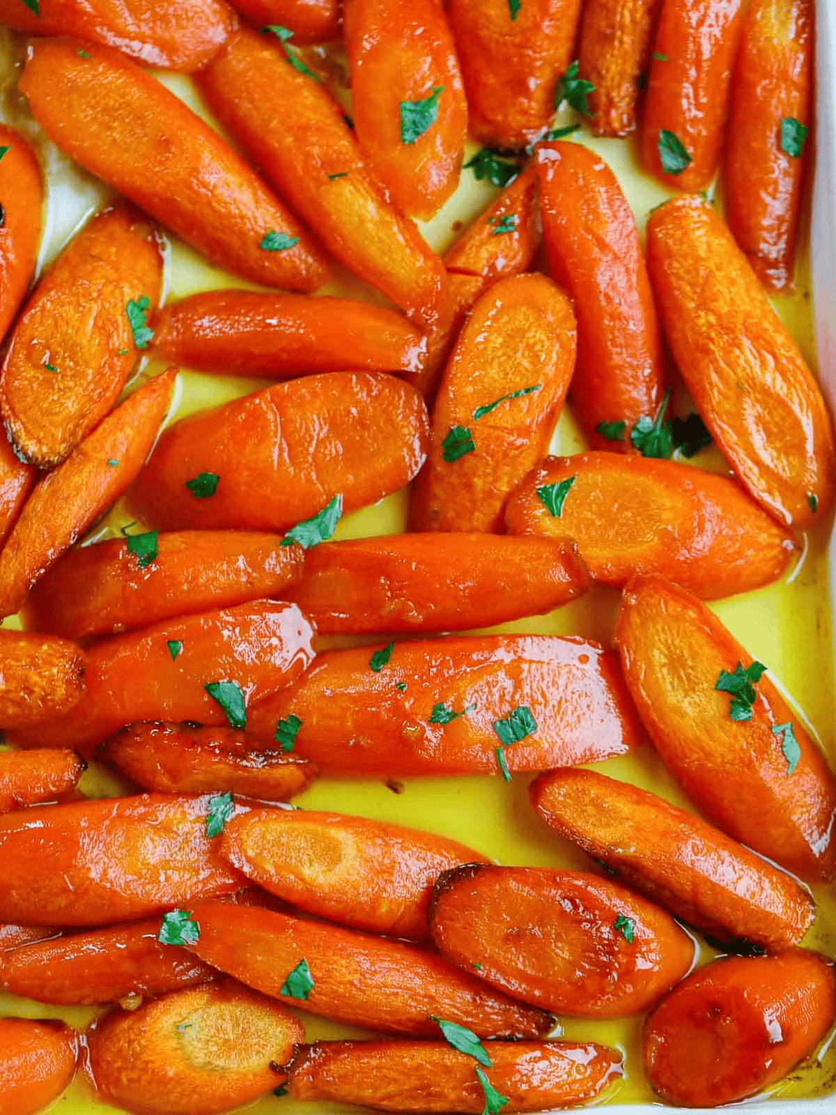 Glazed carrots with browned edges and chopped parsley in a white oval dish.