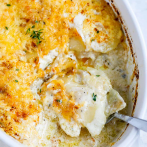 A spoon scooping creamy potato gratin from the baking dish.