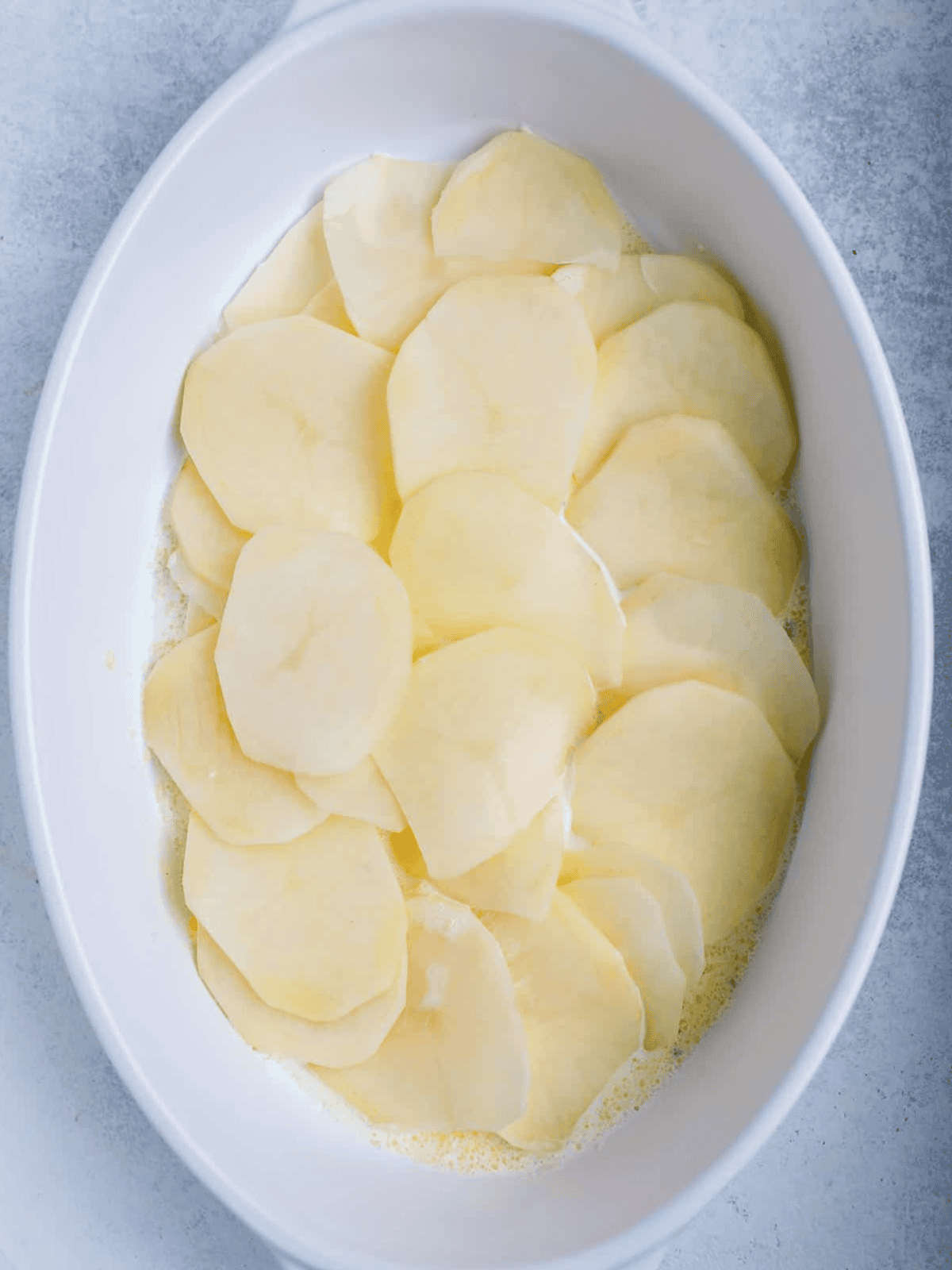 Thin potato slices layered in a buttered baking dish.