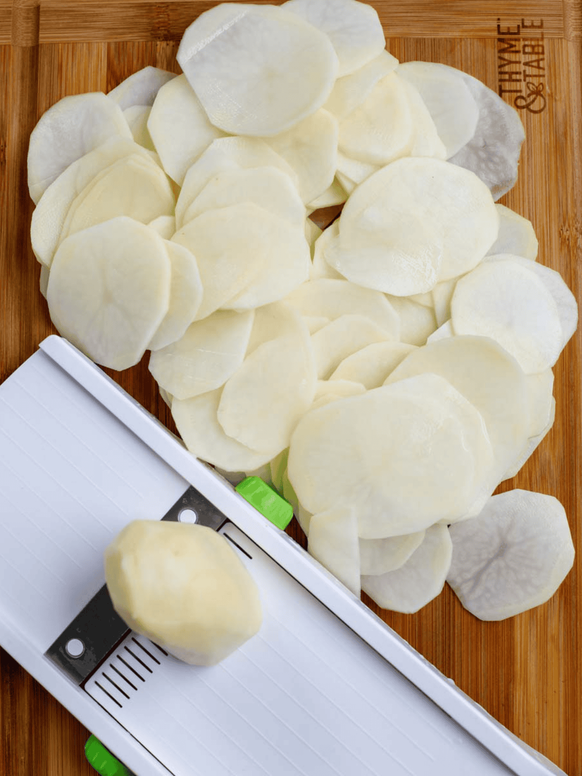 Thin potato slices prepared with a mandoline on a wooden board.
