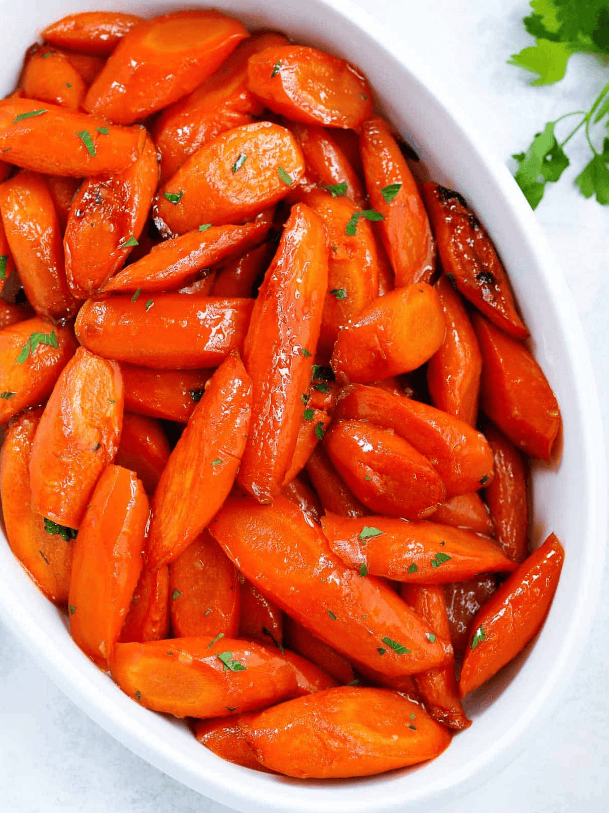 Brown Sugar Glazed Carrots Roasted glazed carrots topped with parsley in a white serving dish.