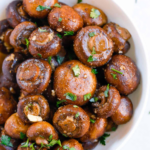 Oven-roasted garlic mushrooms served in a white bowl with chopped parsley.