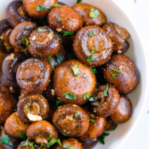 Oven-roasted garlic mushrooms served in a white bowl with chopped parsley.
