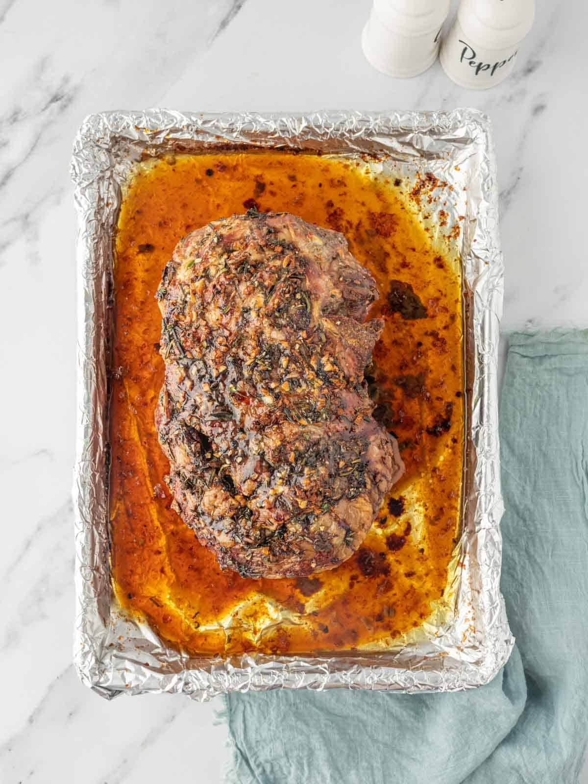 Garlic and herb lamb roast on a foil-lined baking sheet with pan drippings.
