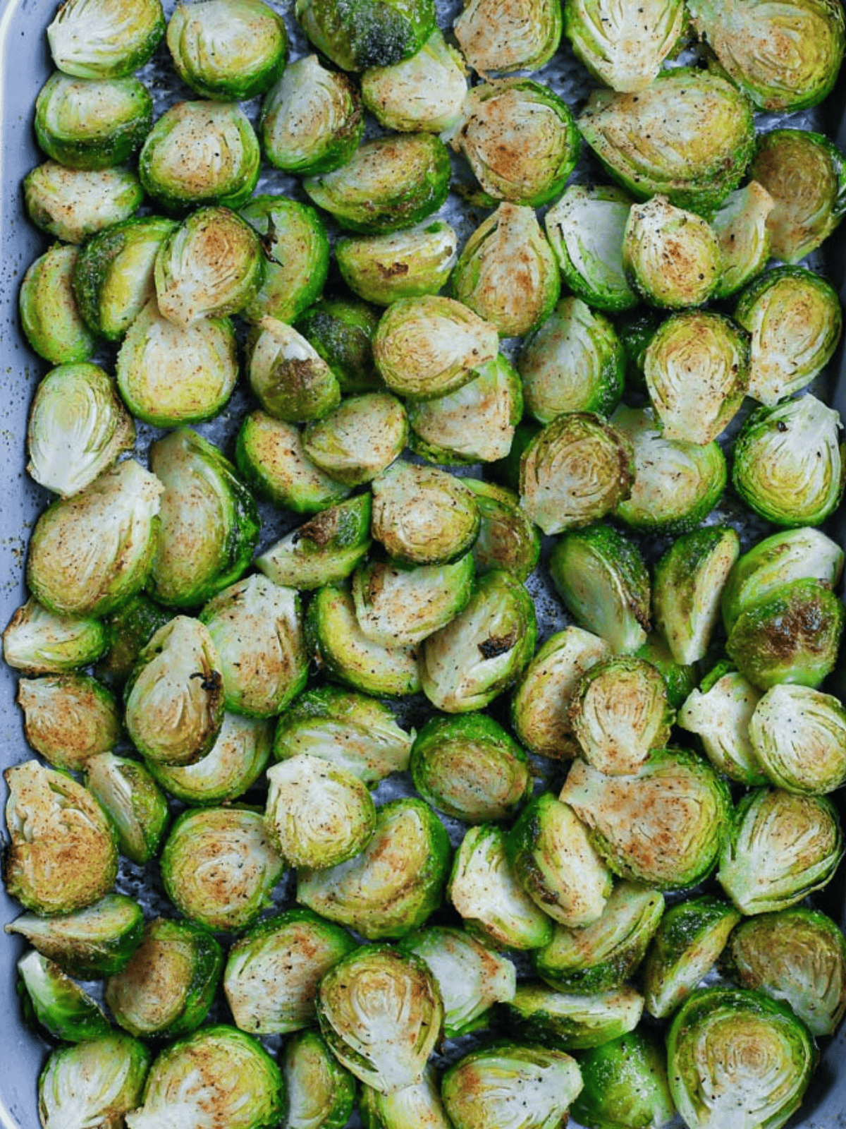 Brussels sprouts seasoned with spices and spread across a baking pan.