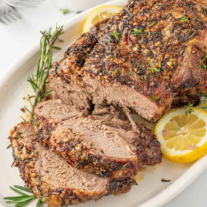 Sliced leg of lamb with a garlic and herb crust, fresh rosemary, and lemon.