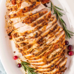Sliced roasted turkey breast with golden seasoned skin, rosemary, and cranberries.