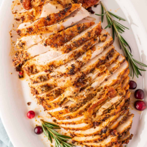 Sliced roasted turkey breast with golden seasoned skin, rosemary, and cranberries.