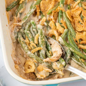 A spoon scooping creamy green bean casserole with crispy fried onions from the baking dish.