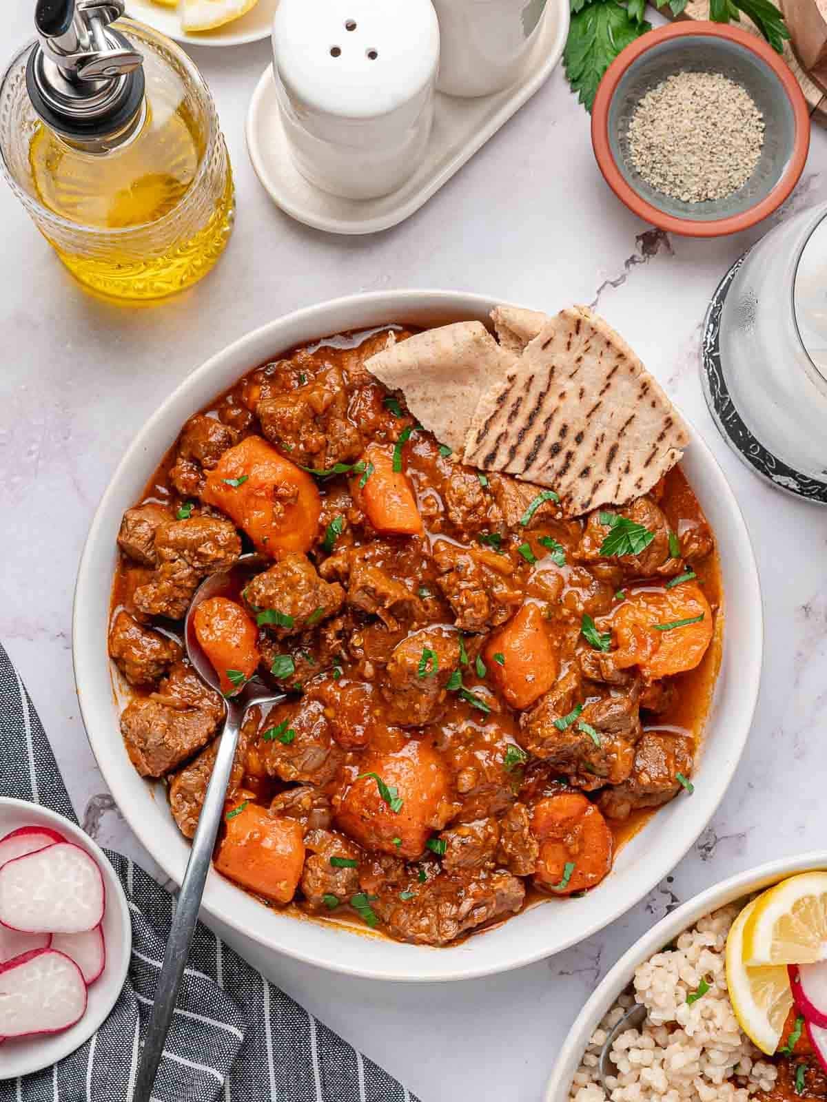 Tomato beef stew served on a platter with flatbread.