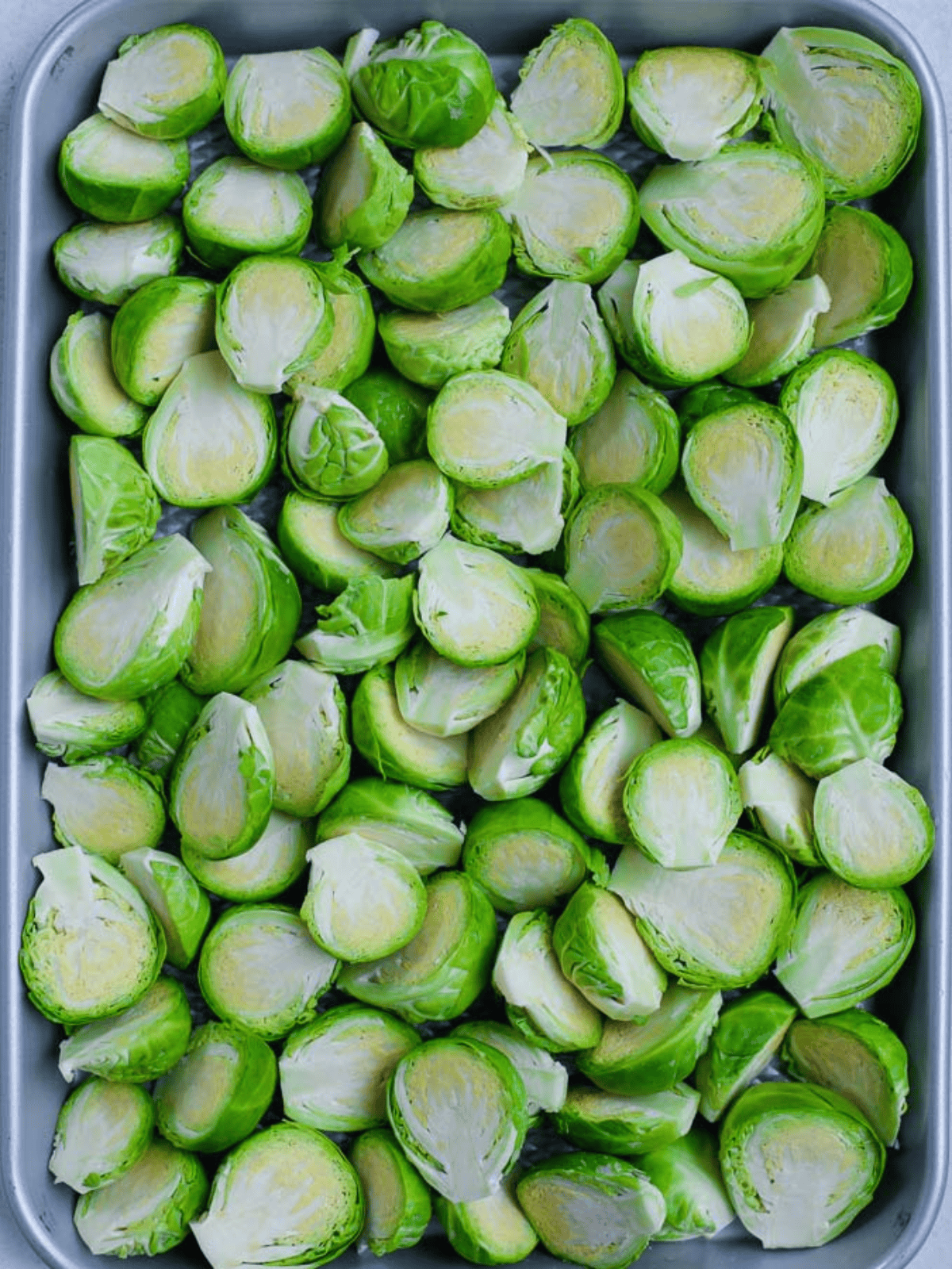Halved and trimmed Brussels sprouts arranged on a baking pan.