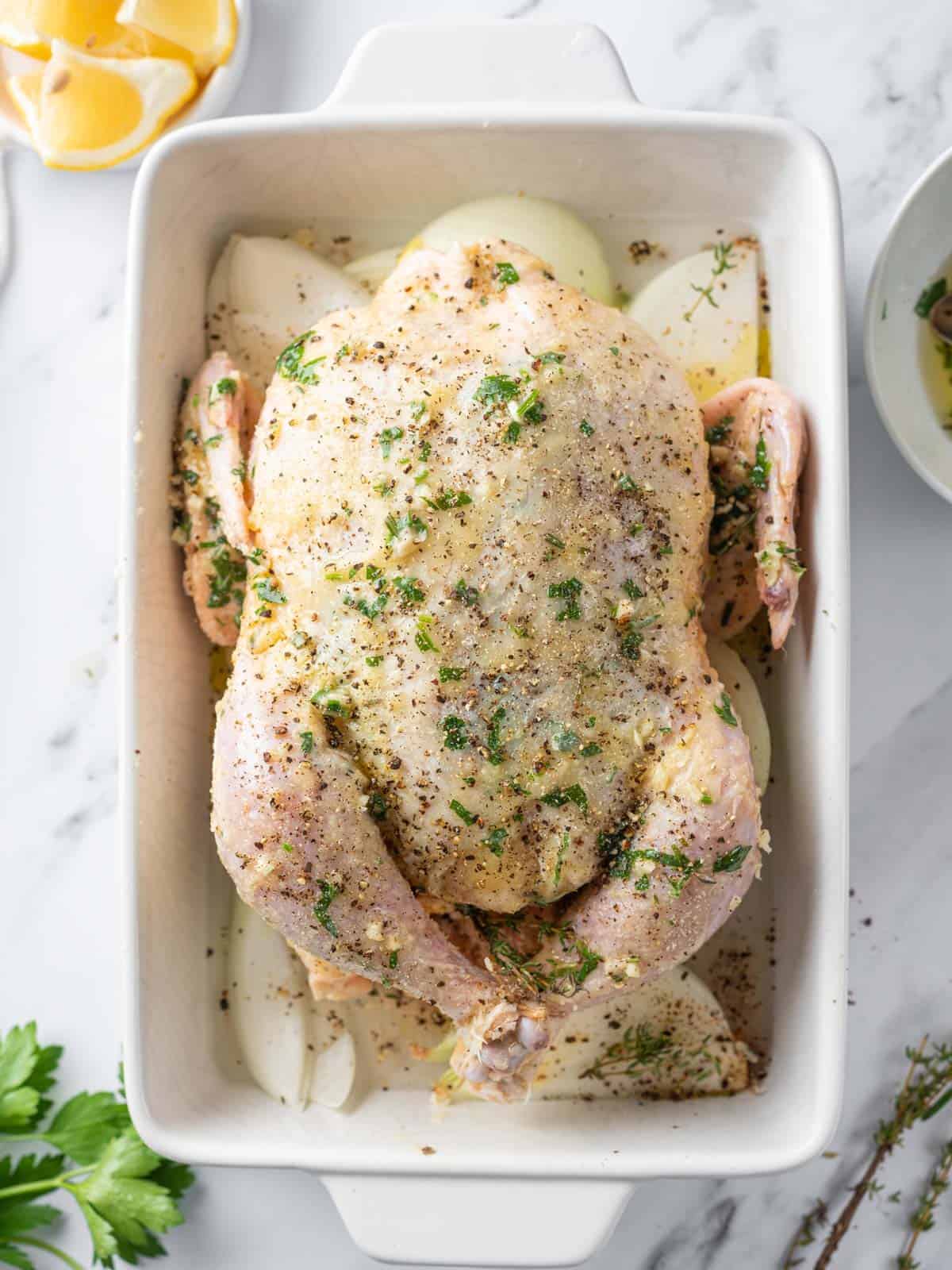 Whole chicken coated with garlic herb butter over onion wedges.