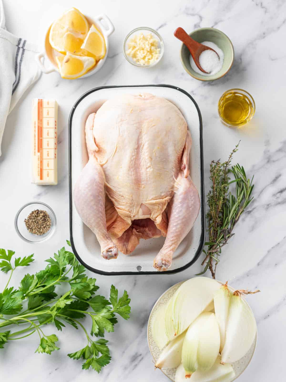 Whole raw chicken with butter, garlic, herbs, lemon, onion, oil, salt, and pepper.