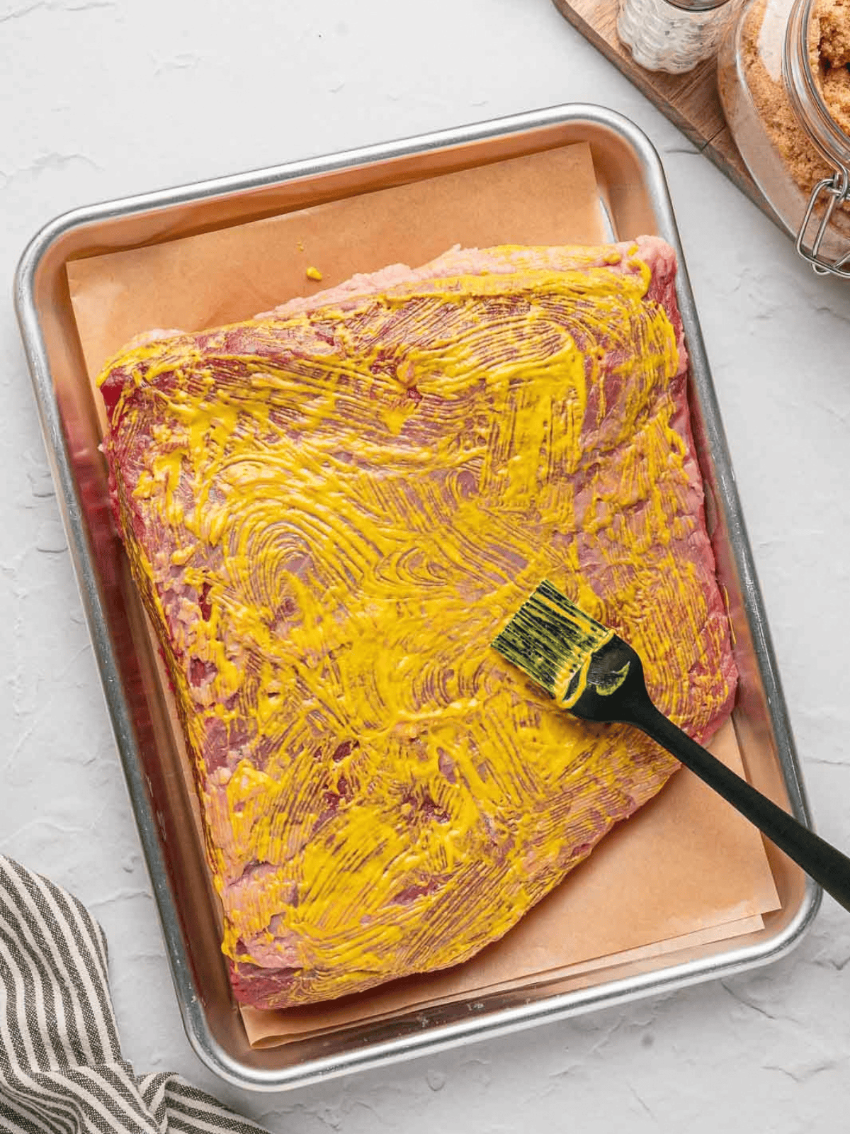 Raw beef brisket coated with yellow mustard before seasoning.