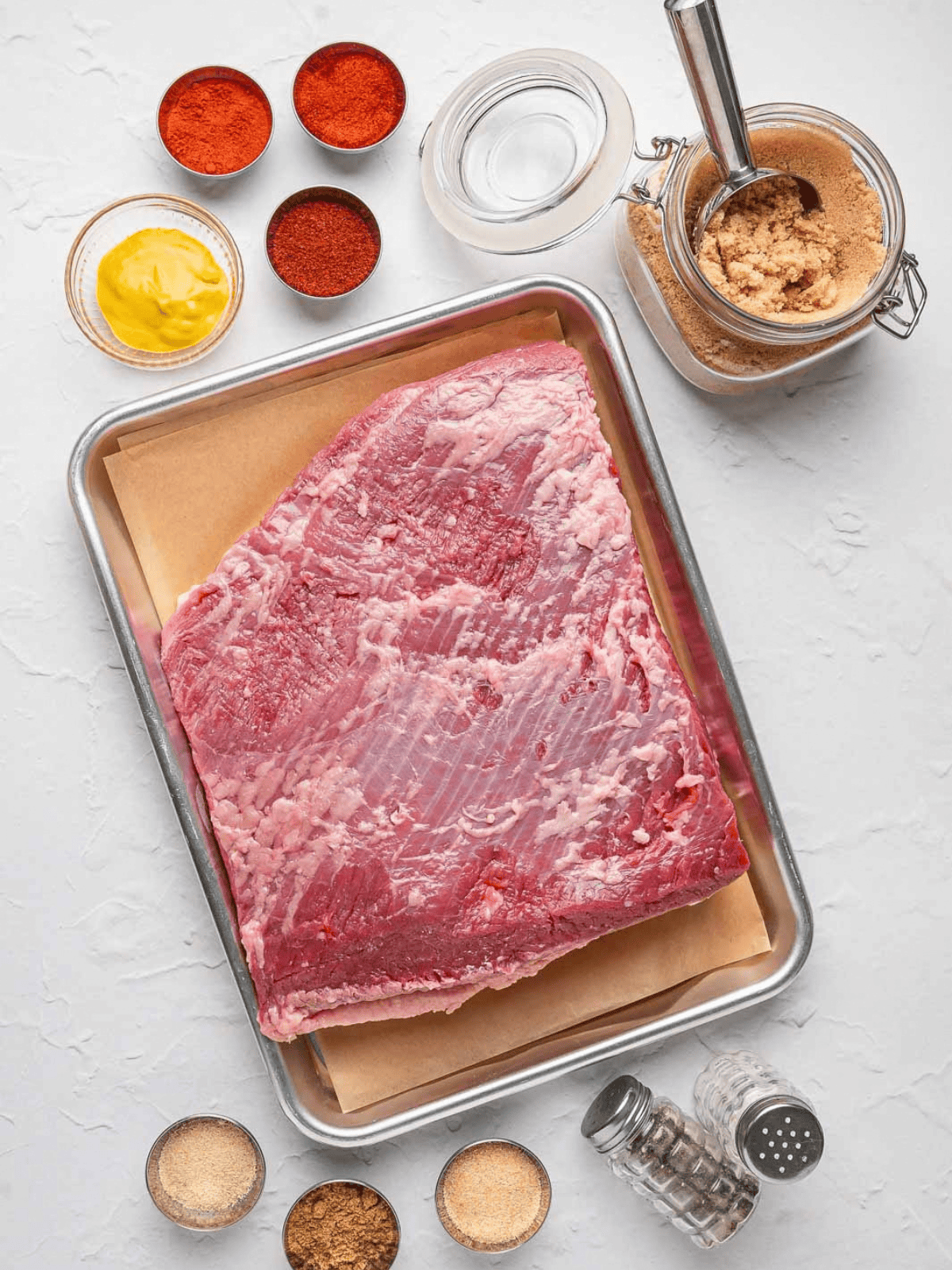 Raw beef brisket with mustard, brown sugar, and dry rub seasonings.